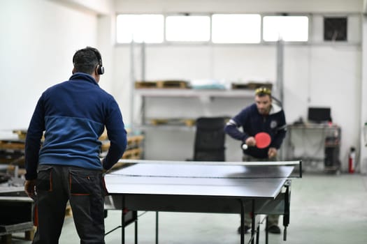 group of industry workers playing ping pong or table tennis game and relaxing in their free time at modern creative metal industry production factory