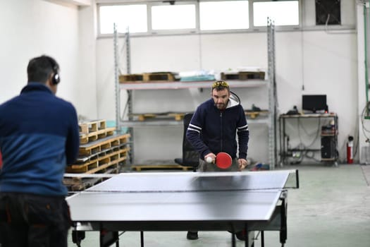 group of industry workers playing ping pong or table tennis game and relaxing in their free time at modern creative metal industry production factory