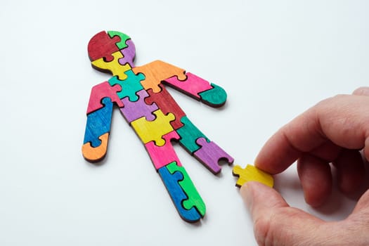A hand assembles figure from multi-colored puzzles as a concept of autism.
