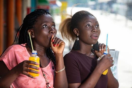 Young girls standing outdoors looking at something up there surprises with shopping bags and bottles of juice in hand.