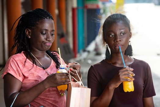 Young girls standing outdoors drinking fruit juice with shopping bags in hand.