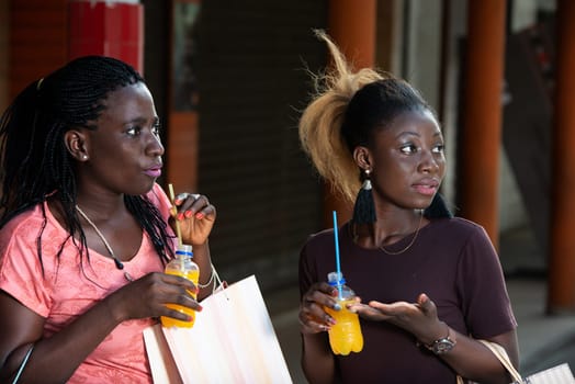 Young girls standing outdoors with bottles of fruit juice watching something after shopping.