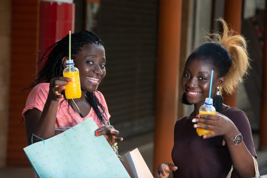 Young girls standing outdoors showing bottles of fruit juice after shopping while smiling.