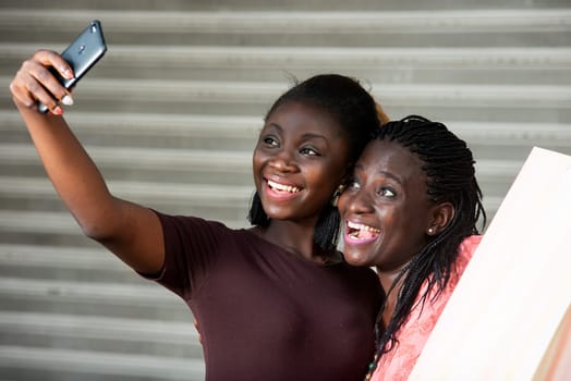 Two young friends taking a picture of themselves on a smart phone smiling.