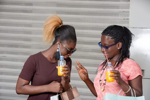 Young girls standing in sunglasses chatting with bottles of juice in hand after shopping.