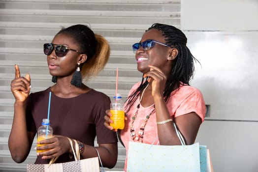 Young girls standing in sunglasses chatting smiling with bottles of juice in hand after shopping.