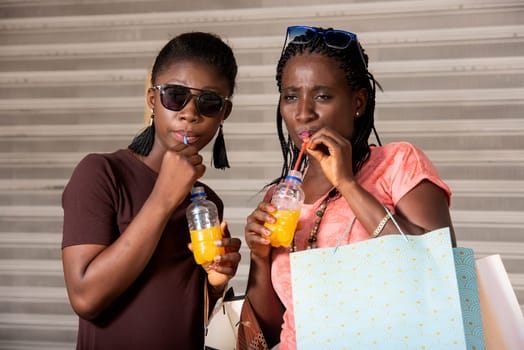young girls standing in sunglasses drinking fruit juice after shopping.