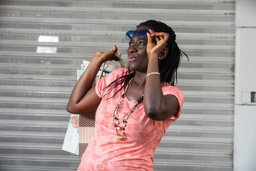 young woman standing outside in sunglasses carrying shopping bags and watching something while stifling.