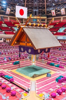 tokyo, ryogoku - jan 14, 2023: The sumo wrestling dohyō of the Kokugikan Arena, with a Japanese Shinto Tsuriyane roof adorned with a hinomaru national flag hanging above the empty arena after a match.