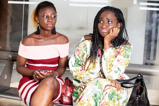 two young women sitting in a waiting room impatiently.