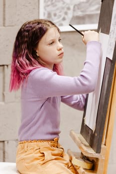 Girl 11 years old craftswoman are painting on canvas in studio standing in front of easel. Portrait of a girl painting during an art class