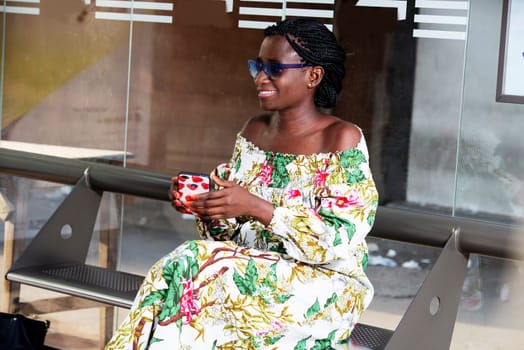 young woman sitting in sunglasses smiling with mobile phone in hand.