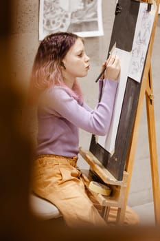 Girl 11 years old craftswoman are painting on canvas in studio standing in front of easel. Portrait of a girl painting during an art class