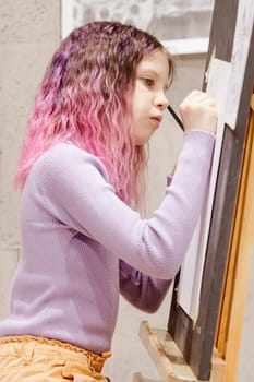 Girl 11 years old craftswoman are painting on canvas in studio standing in front of easel. Portrait of a girl painting during an art class