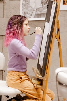 Girl 11 years old craftswoman are painting on canvas in studio standing in front of easel. Portrait of a girl painting during an art class