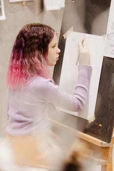 Girl 11 years old craftswoman are painting on canvas in studio standing in front of easel. Portrait of a girl painting during an art class