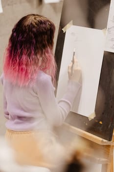 Girl 11 years old craftswoman are painting on canvas in studio standing in front of easel. Portrait of a girl painting during an art class