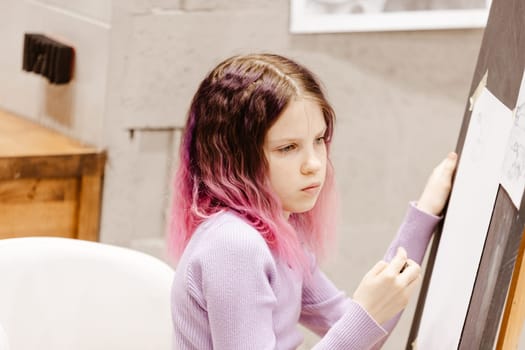 Girl 11 years old craftswoman are painting on canvas in studio standing in front of easel. Portrait of a girl painting during an art class