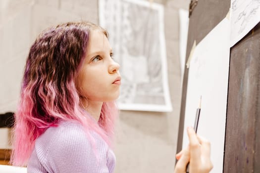 Girl 11 years old craftswoman are painting on canvas in studio standing in front of easel. Portrait of a girl painting during an art class