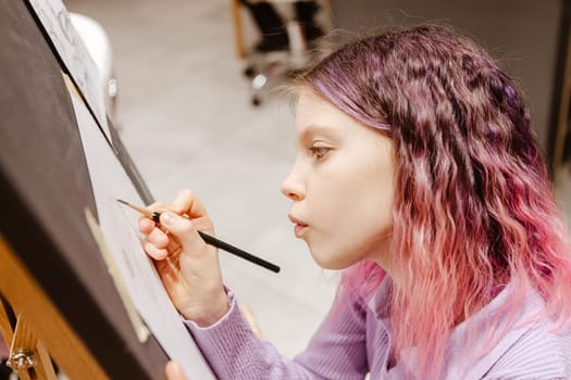 Girl 11 years old craftswoman are painting on canvas in studio standing in front of easel. Portrait of a girl painting during an art class