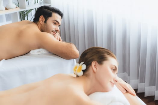 Caucasian couple customer enjoying relaxing anti-stress spa massage and pampering with beauty skin recreation leisure in day light ambient salon spa at luxury resort or hotel. Quiescent