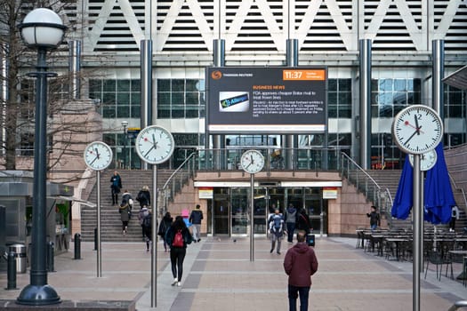 London, United Kingdom - February 03, 2019: People walk under Six Public Clocks - famous art design by Konstantin Grcic at Canary Wharf. Every of 12 clocks shows different numeral