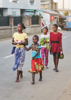 Ranohira, Madagascar - April 29, 2019: Group of four unknown young Malagasy girls wearing bright coloured clothes walking barefoot in evening on the main street of Ranohira