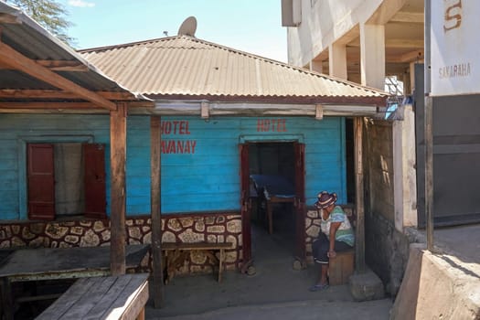 Sakaraha, Madagascar - May 05, 2019: Anonymous Malagasy woman in hat sitting in front of her house advertised as HOTEL. Many locals offer cheap accommodation in their homes, to earn some money