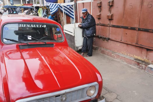 Antananarivo, Madagascar - April 24, 2019: Bright red vintage Renault 4 parked on the main street, unknown barefoot older Malagasy man in background. Most of cars on Madagascar are cheaper older ones