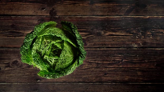 Top down view, single raw savoy kale cabbage on dark wooden board, wide banner space for text right side