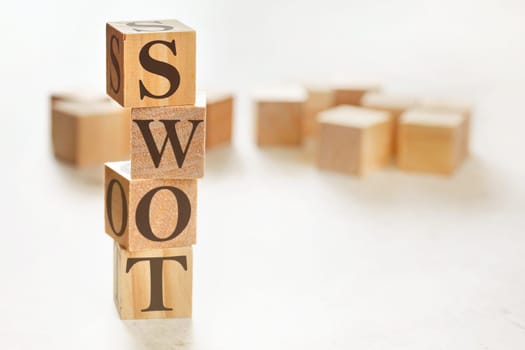 Four wooden cubes arranged in stack with text SWOT (meaning Strengths, Weaknesses, Opportunities and Threats) on them, space for text / image at down right corner