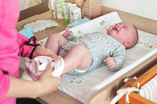 Four months old infant baby boy at changing table, crying as mother is putting his clothed on him