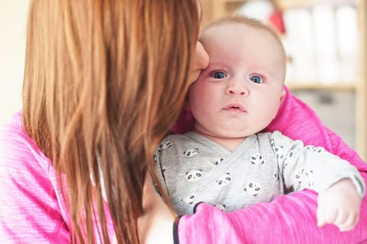 Mother holding her infant baby son, kissing him on face from side