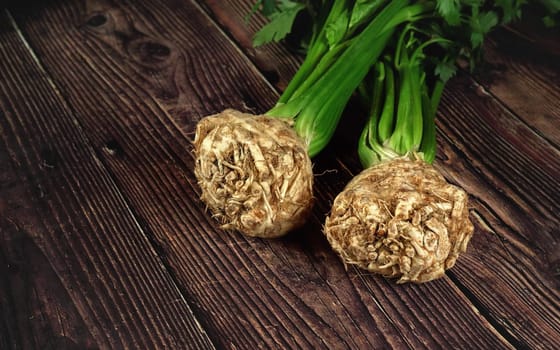 Two celery roots with green leaves on dark wooden board