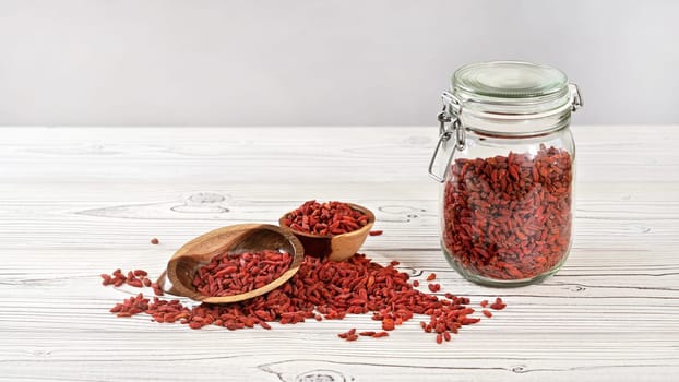 Dried goji aka. wolfberry inside glass jar bottle, some in wooden bowls and spilled on white boards desk, space for text up left corner