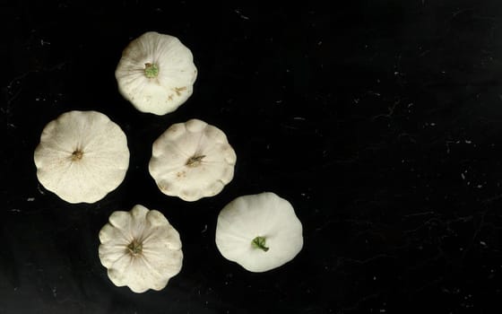 Top down view, five white pattypan squashes on dark marble like board, space for text right side