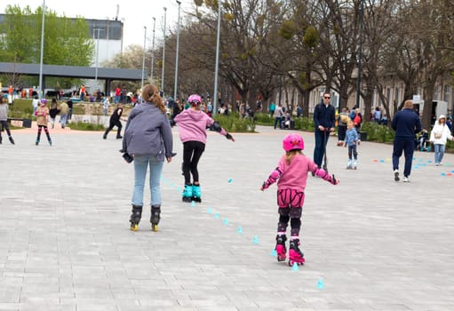 Ukraine. Kyiv. 23.04.2023. children, teenagers playing roller skates with friends outdoors. lot of children, kids go rollerblading, learn roller-skating with an adult instructor, having break in shade