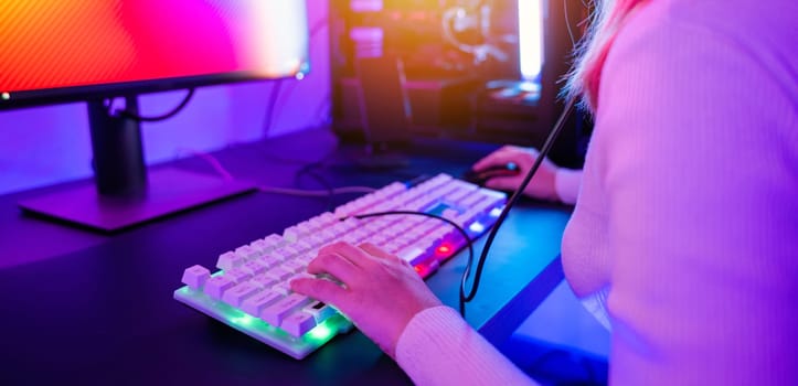 Close up hand of gamer playing cyber video game online with personal computer keyboard at home, woman actively pushing gaming keyboard buttons in the neon room