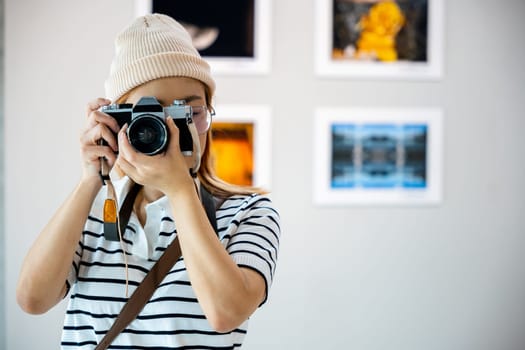 Photographer look viewfinder of her camera at front photo frame show exhibit artwork gallery, Asian woman takes picture art gallery collection in framed paintings pictures on white wall with camera