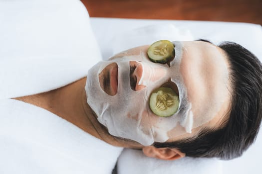 Serene daylight ambiance of spa salon, man customer indulges in rejuvenating with luxurious cucumber facial mask. Facial skincare treatment and beauty care concept. Quiescent