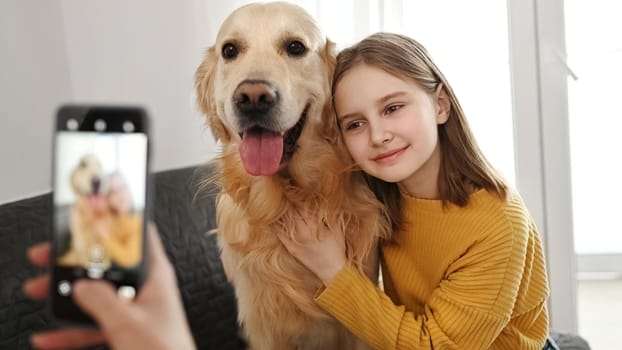 Girl hand with smartphone taking photo of golden retriever dog and preteen child kid at home. Woman mother photograph shoting pet doggy and daughter with mobile phone camera