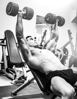 Strong muscular bodybuilder man pressing dumbbells on an inclined bench