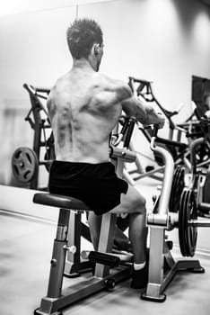 Strong muscular bodybuilder man doing back with the seated row machine in a modern gym