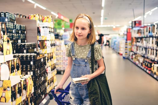 Pretty girl child buying with shopping list in supermarket. Beautiful female preteen kid in liquor department with drink diversity