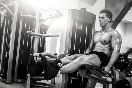 Strong muscular man doing legs with machine in a modern gym