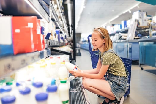Pretty girl child choosing milk in supermarket shop. Beautiful female preteen kid looking lactose latte products in grocery store