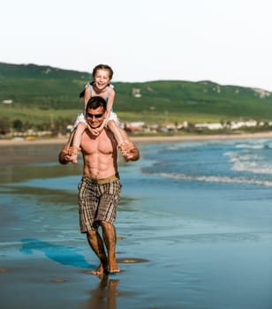 Father holding daughter at shoulders at sea coast and running. Family dad and pretty smiling child kid at beach at summer