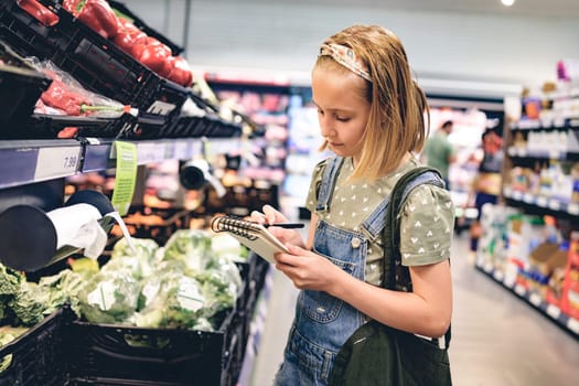 Pretty girl child buying with shopping list in supermarket and looking productson shelf. Beautiful female preteen kid in grocery store
