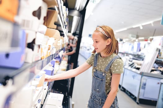 Pretty girl child choosing yogurt in supermarket. Beautiful female preteen kid looking milk products in grocery store