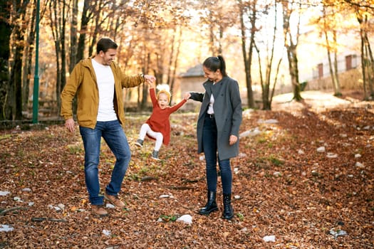 Mom and dad raise a little girl high by the arms, standing in the autumn forest. High quality photo
